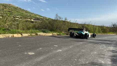 Race-Cars-Passing-By-The-Road-Track-At-The-Hill-In-Imtahleb-Malta-On-A-Bright-Sunny-Weather---Closeup-Shot