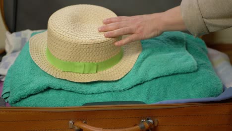 Woman-putting-straw-hat-into-suitcase-medium-shot