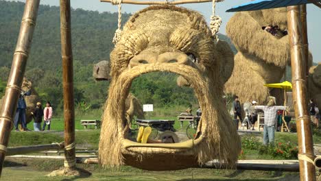 Fun-on-a-King-Kong-head-swing-at-the-Straw-sculptures-park-in-Chiang-Mai,-Thailand-surrounded-by-a-beautiful-landscape-and-lush-green-mountains