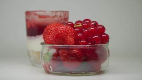 Ein-Köstlicher-Erdbeerkuchen-In-Einem-Glas-Und-Ein-Paar-Erdbeeren-Und-Rote-Johannisbeeren-In-Einer-Durchsichtigen-Schüssel-–-Nahaufnahme