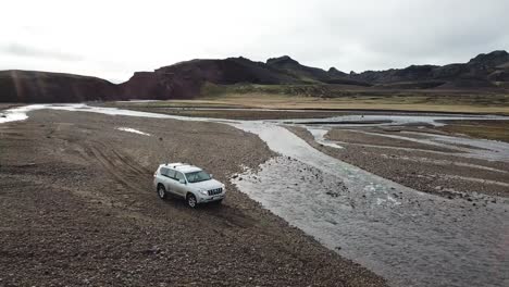 Vehículo-Todoterreno-De-Cuatro-Ruedas-En-El-Desierto-De-Las-Tierras-Altas-Islandesas,-Vista-Aérea-Del-Cruce-De-Cuatro-Ruedas-Sobre-El-Arroyo-Glacial