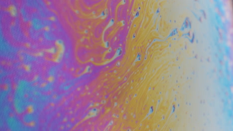 Makroaufnahme-Kleiner-Zellen,-Die-Sich-Auf-Einer-Viskosen,-Regenbogenfarbenen-Flüssigkeit-Auf-Der-Rechten-Seite-Des-Bildes-Zu-Einem-Hellen-Fleck-Bewegen