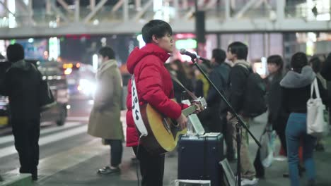 Un-Guitarrista-Masculino-Tocando-En-La-Calle-Fuera-De-La-Estación-De-Shinjuku-En-Tokio,-Japón-Por-La-Noche---Toma-De-Cámara-Lenta-Media