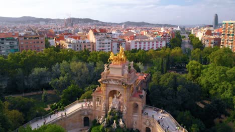 Vista-Aérea-De-La-Cascada-Monumental-Estatua-Dorada-Y-Fuente,-En-El-Parque-De-La-Ciutadella,-Barcelona,-España,-Durante-La-Puesta-De-Sol---Reversa,-Tiro-Con-Drones