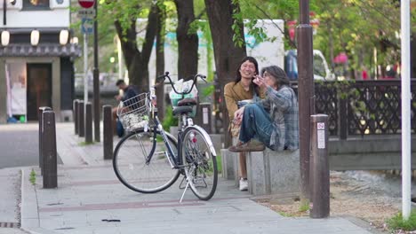 Zwei-Japanische-Freunde-Sitzen-Auf-Der-Betonbank,-Unterhalten-Sich-Und-Haben-Eine-Gute-Zeit-Beim-Rauchen-Auf-Der-Straße-In-Kyoto,-Japan