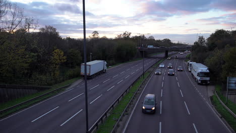 A-time-lapse-overlooking-vehicles-with-headlights-on-travelling-on-a-triple-lane-road-and-passing-under-a-flyover-at-dusk-on-a-cold-November-day