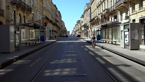 Opera-trolley-empty-stop-at-Cours-de-Intendance-avenue-with-man-in-bicycle-signaling-passing-by-during-the-COVID-19-pandemic,-Dolly-forward-walking-shot