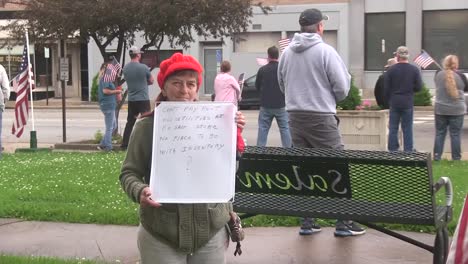 Old-Caucasian-woman-stands-on-street-holding-up-protest-sign-with-letters,-covid-19-pandemic,-static-zoom-out