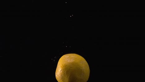 Slow-motion-clip-of-an-orange-with-black-background-being-dropped-into-water-inside-a-fish-tank