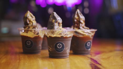 Three-Cups-Of-Chocolate-Sundae-On-Wooden-Table-With-Bokeh-Lights-In-Background-In-Black-Scoop-Cafe,-Philippines