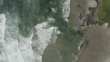 Left-to-right-green-and-blue-ocean-waves-crashing-into-ocean-shore,-peaceful-drone-video