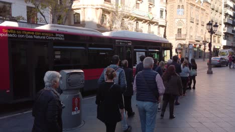 Long-line-of-people-getting-on-bus-at-bus-stop-in-Spain,-Slow-Motion