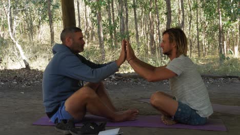 Dos-Hombres-Sentados-En-La-Alfombra-De-Yoga-Uno-Frente-Al-Otro-Haciendo-Ojo-A-Ojo---Palma-A-Palma-Como-Conexión---Queensland,-Australia