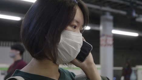 Mujer-Japonesa-De-Pelo-Corto-Con-Mascarilla-Quirúrgica-Hablando-En-Su-Teléfono-Inteligente-En-Tokio,-Japón-Durante-La-Pandemia