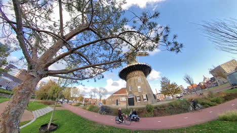 Vista-De-Pez-Hacia-Adelante-Del-Histórico-Molino-De-Viento-De-Valk,-Museo-Y-Ciclista-En-La-Ciudad-De-Leiden,-Países-Bajos