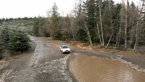 Backtracking-a-Subaru-Crosstrek-through-deep-brown-mud-puddles,-aerial,-illustrative-editorial