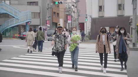 Lugareños-Con-Máscara-Médica-Cruzando-El-Carril-En-La-Carretera-De-La-Ciudad-De-Tokio-En-Japón