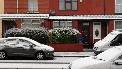 Idyllic-winter-snow-falling-in-street-of-town-houses-and-frozen-parked-cars