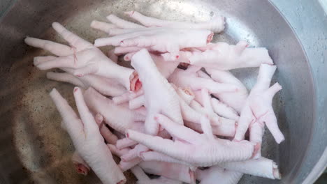Close-up-Inox-pan-with-uncooked-Chicken-feet-on-water,-hand-adding-Chicken-feet-piece
