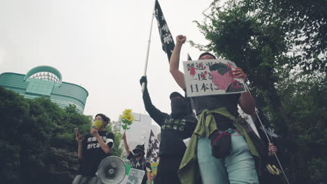 Protesters-With-Megaphone,-Placard,-And-Flag-Marching-And-Shouting-In-The-Street-Of-Tokyo---Solidarity-With-Hong-Kong-Protest-In-Japan---low-angle-shot
