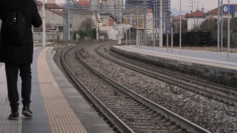 Back-View-of-Man-Walking-Near-the-Train-Rails-at-Station