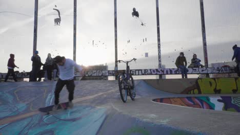 Junger-Mann-Macht-Einen-Heelflip-Mit-Dem-Skate-In-Zeitlupe-In-Einem-Skatepark-Mit-Dem-Sonnenuntergang-Im-Hintergrund