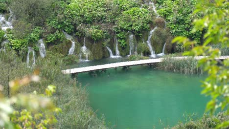 Fernsicht-Auf-Einen-Holzsteg-Entlang-Verschiedener-Wasserfälle-Mit-Ästen-Im-Vordergrund-Im-Nationalpark-Plitvicer-Seen-In-Kroatien,-Europa