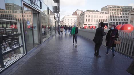 Caminando-Por-Un-Camino-Pavimentado-En-Place-De-La-Monnaie-Con-Personas-Deambulando-En-Medio-De-La-Pandemia-De-Coronavirus-En-Bruselas,-Bélgica---Pov,-Toma-De-Mano