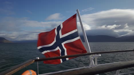 Norwegian-flag-fluttering-in-the-breeze-on-a-boat,-blue-sky-and-clouds