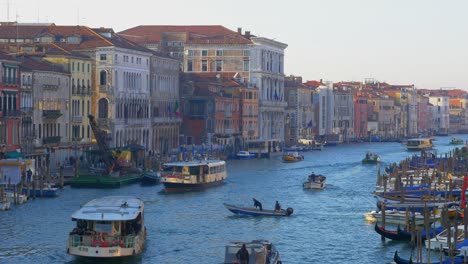 Boat-traffic-on-a-Venice-canal-with-gondolas-and-boats-anchored-to-the-shores-at-sunset