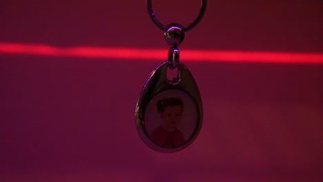 Close-Up-of-the-Hanging-Child's-Photo-in-Metal-Souvenir-Keychain-and-the-Moving-Laser-Light
