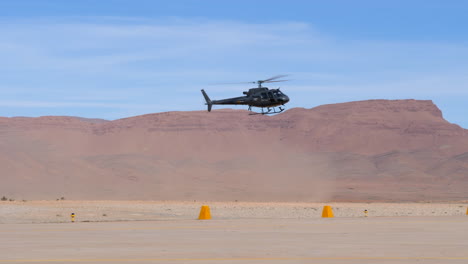 A-helicopter-lands-at-a-desert-airport,-blowing-up-sand-and-dust,-high-mountains-in-de-distance