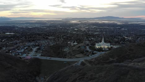 Drone-flies-over-mountains-towards-city,-beautiful-building-in-the-foreground