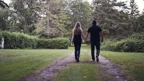 Pareja-Feliz-Tomándose-De-La-Mano-Y-Caminando-Por-Un-Sendero-En-Un-Parque