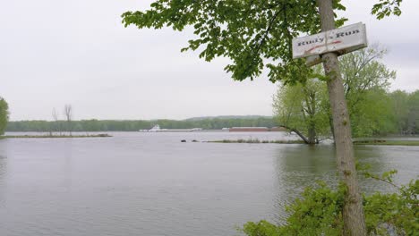 Señalización-Del-Río-Colgando-De-Un-árbol-Junto-Al-Agua-En-Movimiento-En-Un-Día-Nublado-Y-Sombrío,-Rudy&#39;s-Run-La-Crosse-Wisconsin