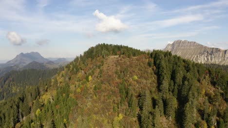 Orbiting-low-in-front-of-high-hill-with-autumn-colors,-alpine-landscape-in-the-background