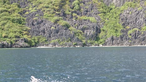 Sailing-in-blue-waters-by-huge-limestone-cliff-with-vegetation-in-El-Nido,-Palawan,-the-Philippines-in-ultra-slow-motion
