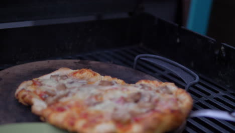 Putting-a-homemade-pizza-out-of-a-wood-fired-pizza-grill-oven