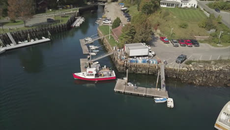 A-red-fishing-boat-unloading-its-catch-in-Rockport-Harbor,-Maine-DRONE