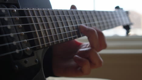 Man-Practising-a-vintage-black-electric-guitar,-rehearsing-chords,-solos-and-octaves-in-a-natural-light-environment.