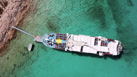 Rotating-Aerial-Shot-of-Day-Cruise-Boat-Docked-at-Balos-Beach-in-Crete,-Greece-in-Beautiful-Turquoise-Water-on-Sunny-Day