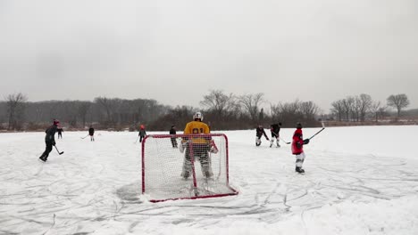 A-view-behind-the-pond-hockey-goalie-of-the-entire-field-as-adults-and-children-play-pond-hockey