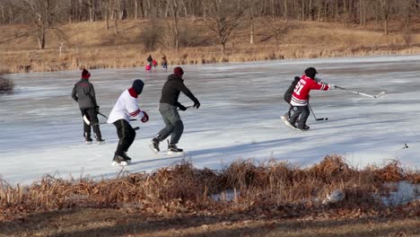 A-wider-angle-shot-of-a-few-friends-playing-pond-hockey-during-a-bright-and-sunny-winter-afternoon
