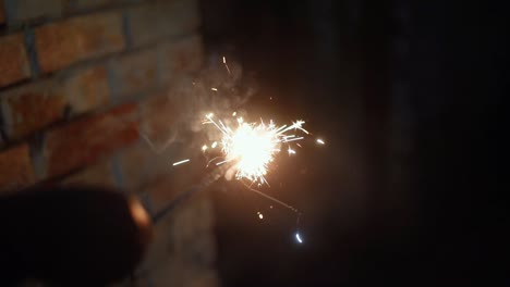 Person's-hand-holding-fire-cracker-at-night,-Slow-motion-with-sparkles-and-smoke-comes-out