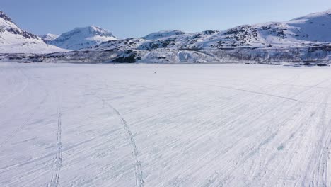 Vista-Aérea-De-Personas-Esquiando-Sobre-Un-Lago-Congelado-En-Un-Paisaje-Montañoso-Nevado