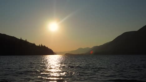 Sonnenuntergang-An-Einem-See-Mit-Bergen-Im-Hintergrund,-Wobei-Ein-Mann-Als-Silhouette-Ins-Wasser-Springt