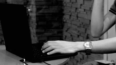 A-male-person-types-on-his-laptop-computer-keyboard-in-a-Philippine-cafe,-with-vehicular-traffic-or-lights-from-outside-showing-through-a-glass-wall