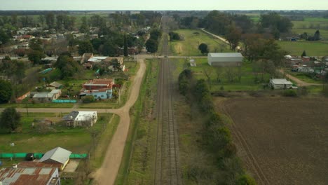 Aerial:-slowly-moving-forward-over-railway-tracks,-afternoon-rural-town,-countryside,-Argentina