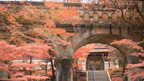 Brick-bridge-surrounded-by-orange-autumn-leaves-in-Kyoto,-Japan-wide-shot-4K