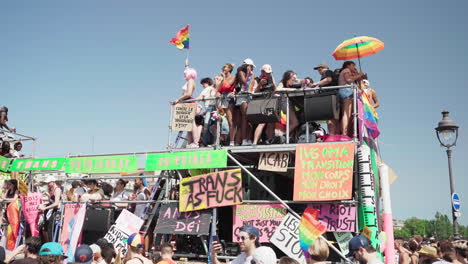 Cerca-De-Gente-De-Fiesta-En-La-Parte-Superior-Y-En-El-Interior-De-Un-Vehículo-Decorado-Con-Colores-Que-Pasa-Por-La-Gente-En-La-Marcha-Del-Orgullo-Gay-En-París,-Francia